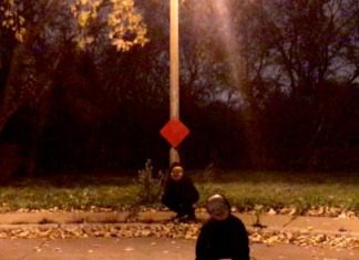 Two people sitting on the ground under a street sign.