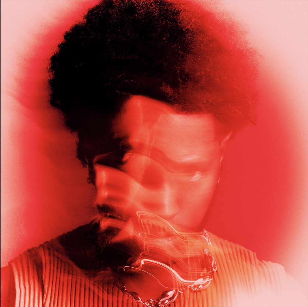 A red-tinted portrait of a man with an afro.