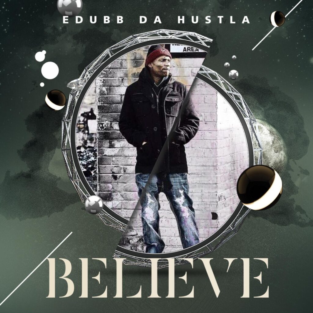 A man standing in front of a brick wall with the text "EDUBB DA HUSTLA BELIEVE"