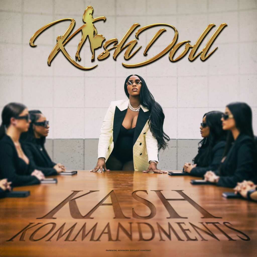 Kash Doll in front of a conference table full of women.